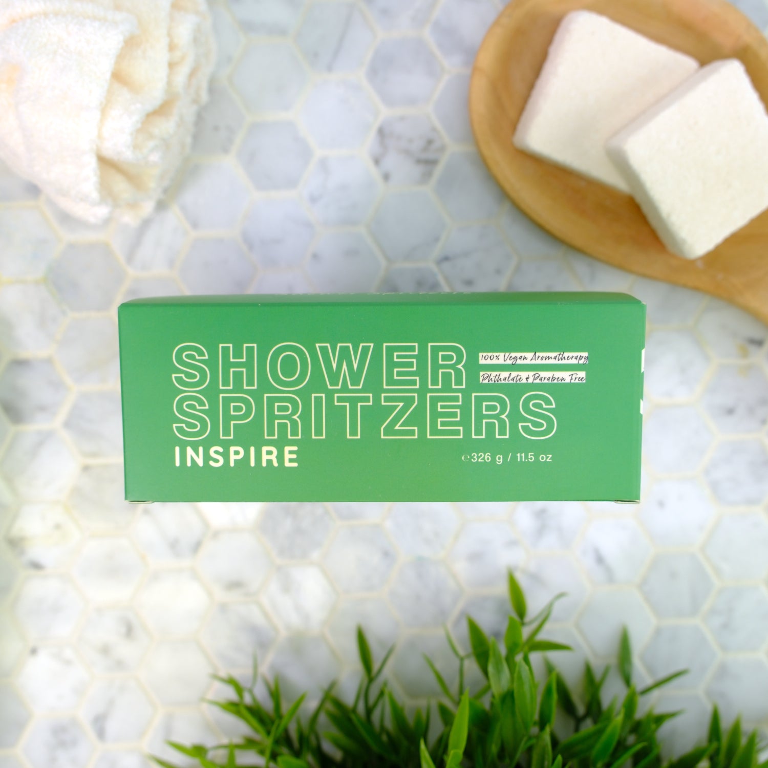 Green box of Shower Spritzers labeled 'Inspire' on a marble surface with spritzers and plants.