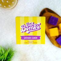 Yellow box of Bath Bombs Lavender Lemon on a white background with bath bombs and a loofah.