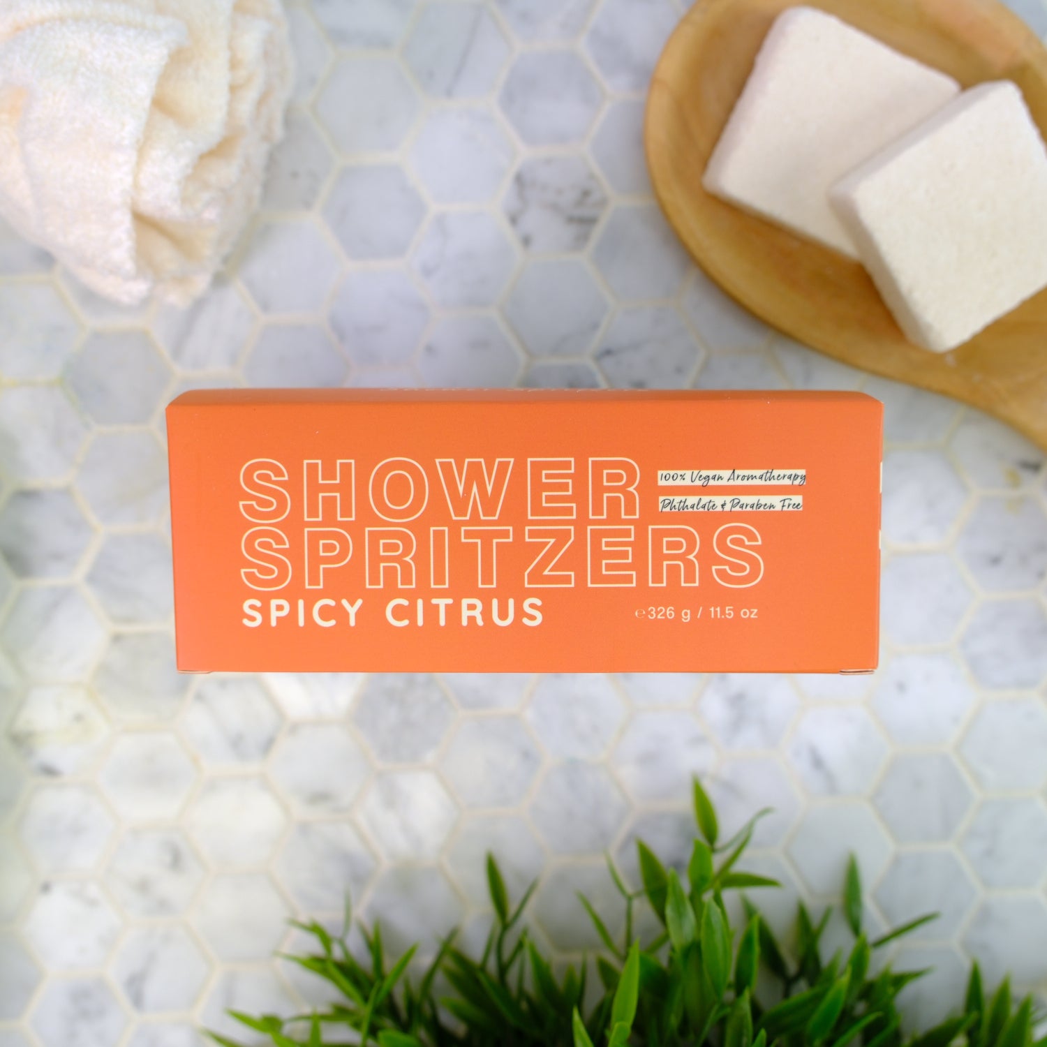 Shower spritzer packaging labeled 'Spicy Citrus' on a marble surface with spritzers and greenery.
